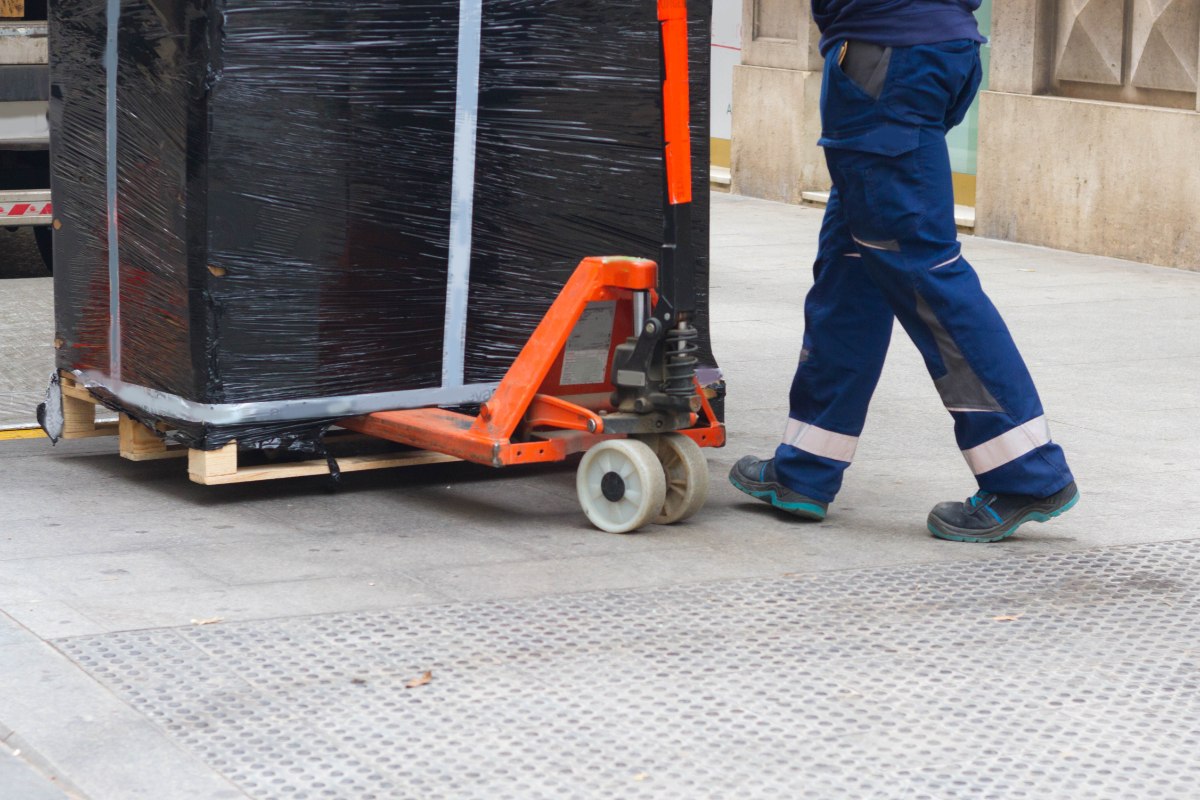 A worker with fork pallet truck stacker in warehouse loading furniture panels